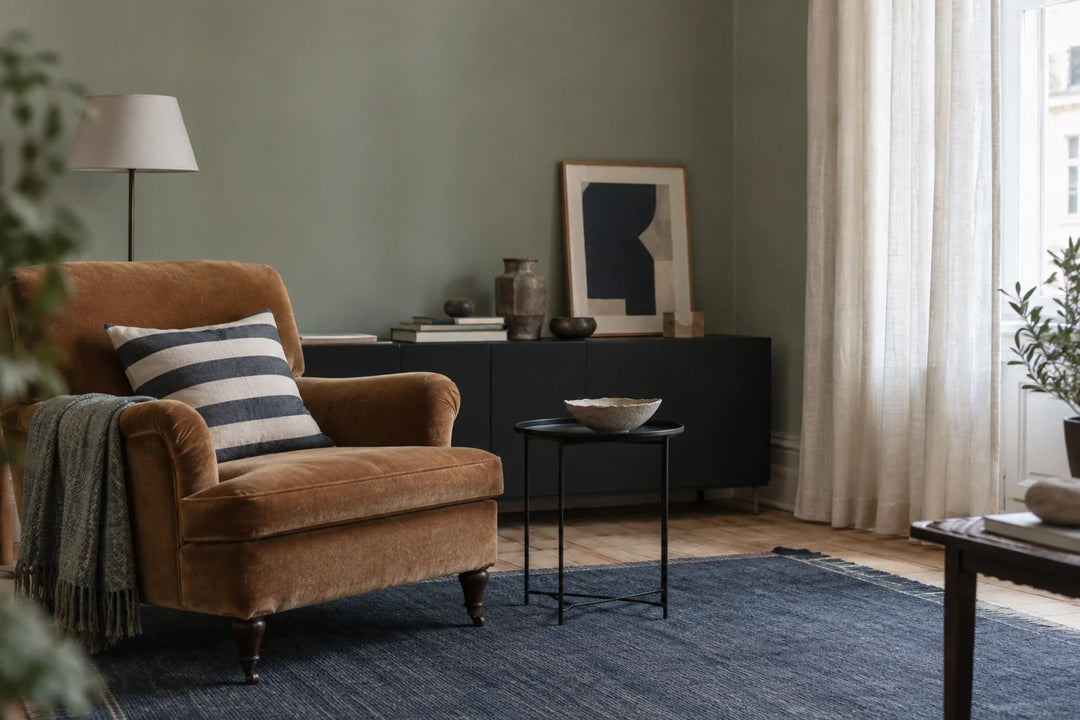 Caramel armchair with a striped cushion, blue rug and linen curtain in soft daylight.