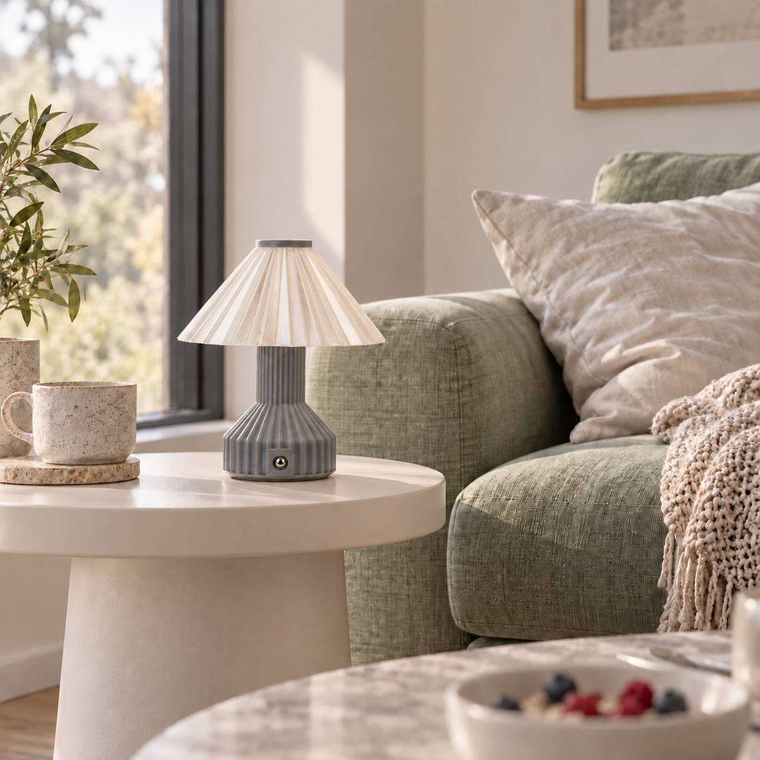 Vela table lamp beside cups on a round table by a green sofa.